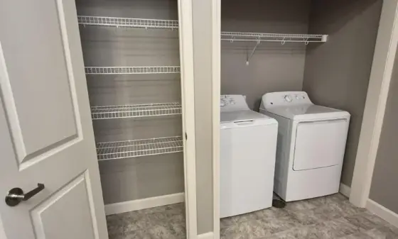 Two open laundry closets: left with empty wire-shelf storage, right with a washer and dryer under a hanging wire shelf.