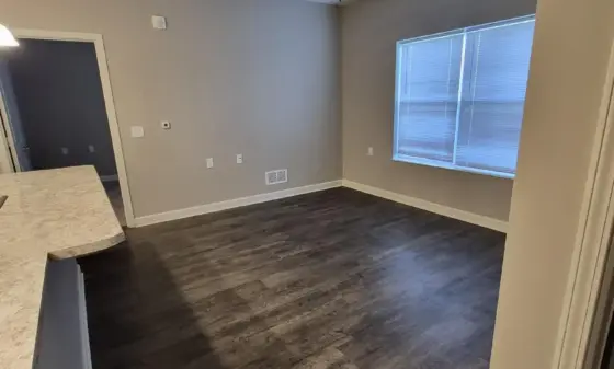 Empty living area with dark wood flooring, gray walls, and a ceiling fan; window with blinds on the right.