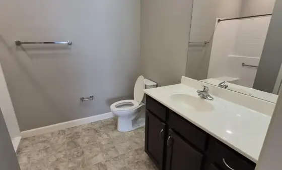 Modern bathroom with a dark wood vanity, white countertop, large mirror, and toilet beside the vanity.