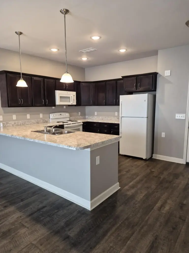 Modern kitchen with dark wood cabinets, white appliances, and a granite island topped with a double sink.