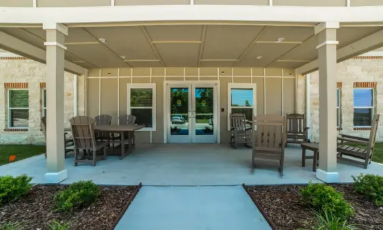 Patio seating area under a covered entrance with brown Adirondack chairs facing a glass double door.