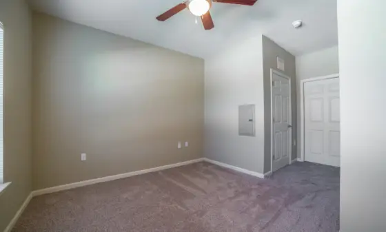 Empty living area with gray walls, beige carpet, and a ceiling fan overhead.