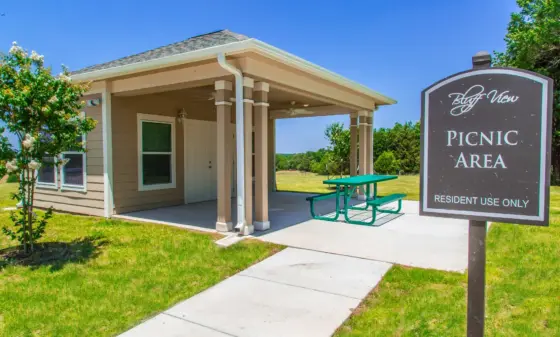 Beige clubhouse with a covered porch and a green picnic table beside a Bluff View Picnic Area sign (residents use only).