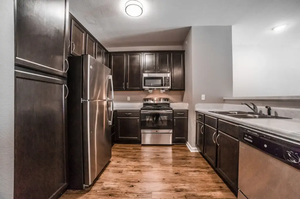 Narrow galley kitchen with dark wood cabinets, stainless steel fridge, range with microwave above, and a dishwasher along the right counter.