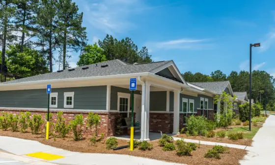 Front view of a single-story building with gray siding and brick base, handicap parking signs by the entrance on a sunny day.