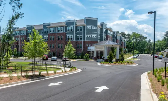 Modern multi-story apartment building with brick lower level and gray siding, under a bright blue sky with trees nearby.