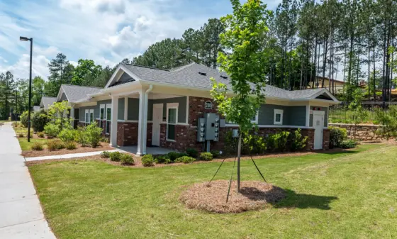 Single-story gray and brick office building with white columns, green lawn, and young trees under a blue sky.