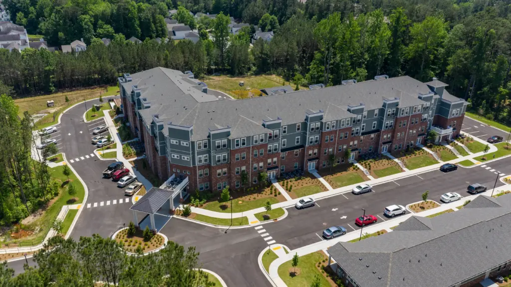 Aerial view of a modern multi-building apartment complex with gray roofs, brick accents, and surrounding trees/grass. - informative image
