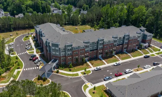 Aerial view of a modern multi-building apartment complex with gray roofs, brick accents, and surrounding trees/grass. - informative image