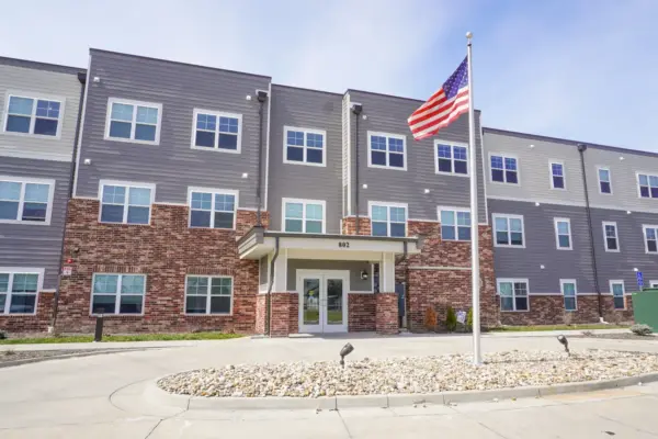 Apartment building with brick base, gray siding, and an American flag on a flagpole in front.] , hmm remove extra comma.