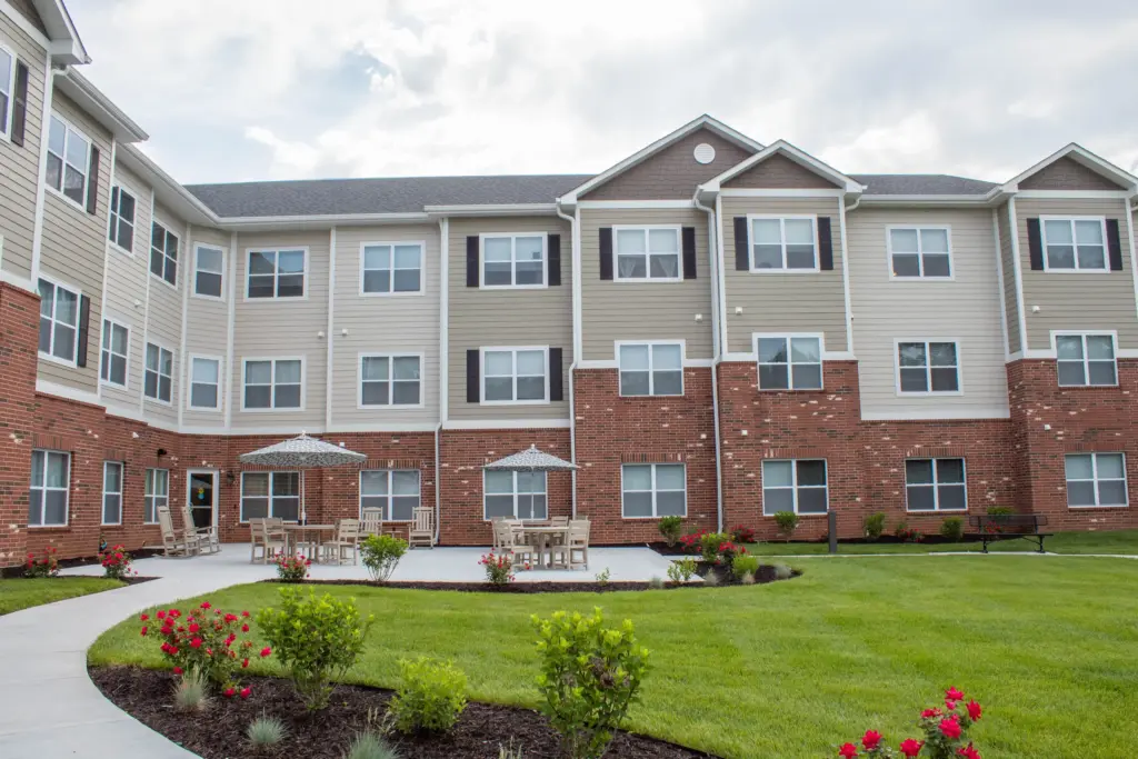Apartment building courtyard with brick base, beige siding, many windows, and outdoor seating under umbrellas.