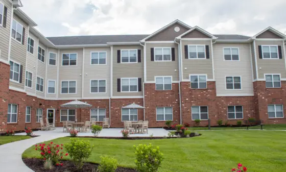 Apartment building courtyard with brick base, beige siding, many windows, and outdoor seating under umbrellas.