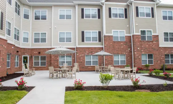 Apartment-style building courtyard with beige siding, brick base, and multiple outdoor tables with umbrellas.