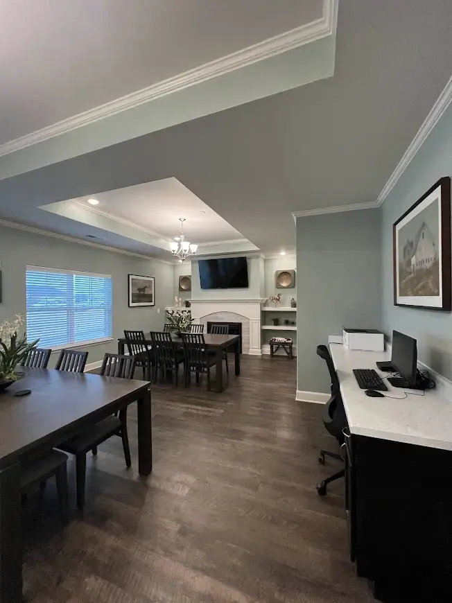 Conference room with two long dark wooden tables and multiple chairs, fireplace and TV on the back wall, soft gray walls, and built-in shelves nearby.