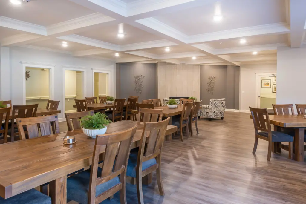 Spacious dining room with wooden tables and chairs, gray walls, and decorative ceiling beams under warm lighting.