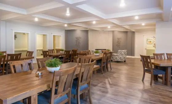 Spacious dining room with wooden tables and chairs, gray walls, and decorative ceiling beams under warm lighting.