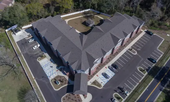 Aerial view of a large brick apartment complex with a central lawn, circular drive, and a small gazebo-shaped pavilion in the courtyard, surrounded by trees and a parking lot nearby