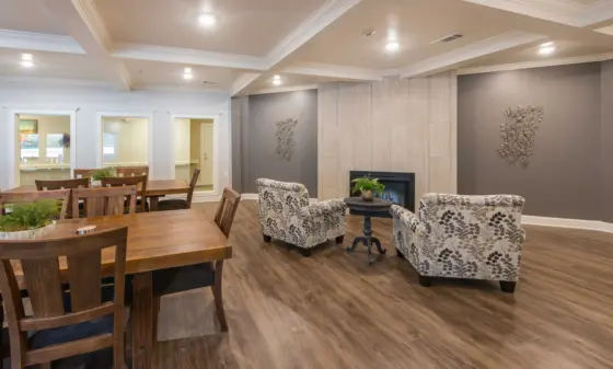 Bright open living/dining area with a long wooden dining table and matching chairs, patterned armchairs, and a stone fireplace on the right.