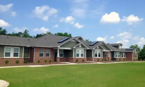 Row of suburban townhomes with brick bases, gray siding, and solar panels on the roofs under a blue sky.