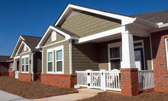 Row of modern suburban homes with brown siding, white trim, and brick bases under a clear blue sky.