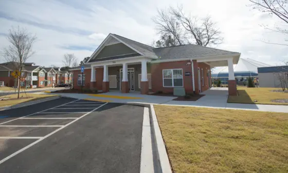 Brick building with a covered entrance and white columns, laundry sign on the side, front parking lot in view.