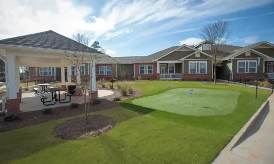 Outdoor courtyard with a covered pavilion, brick buildings, and a small putting green with flags in the lawn area.