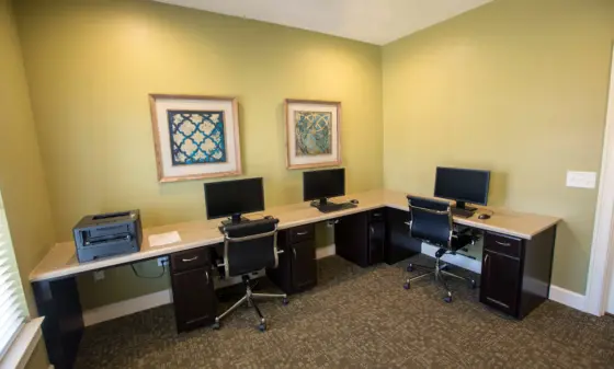 Small office with three computer workstations along a green wall and framed artworks above the desks.