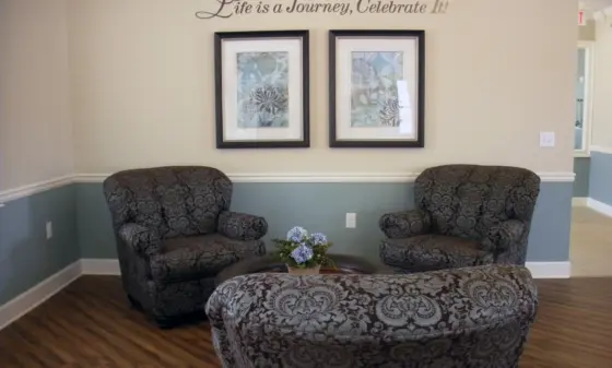 Waiting area with two dark-patterned armchairs, a small coffee table with blue flowers, and wall art reading 'Life is a Journey, Celebrate It!'