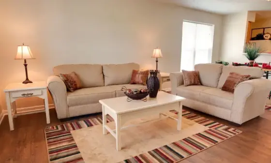 Cozy living room with two beige sofas, a white coffee table, striped area rug, and table lamps on each side.
