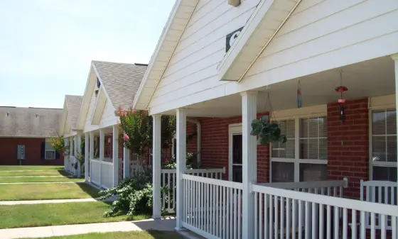 Row of white siding townhouses with peaked roofs, covered porches, white railings, and hanging bird feeders along a green lawn.