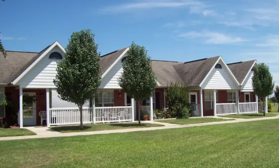 Row of white townhouses with gabled roofs, front porches, and trimmed lawns under a clear blue sky.