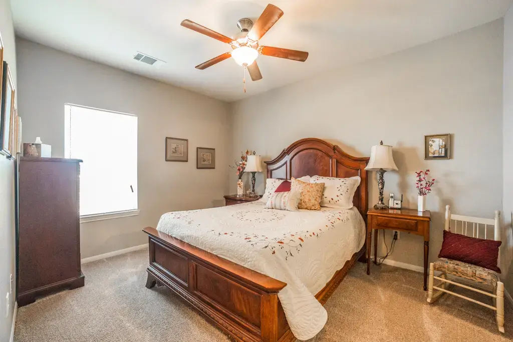 Bedroom with a dark wooden king-size bed, matching nightstands, and a ceiling fan with wooden blades."